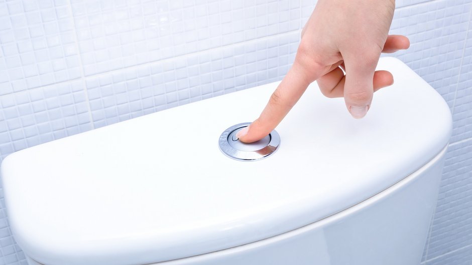 Finger betätigt die Spülung einer Toilette